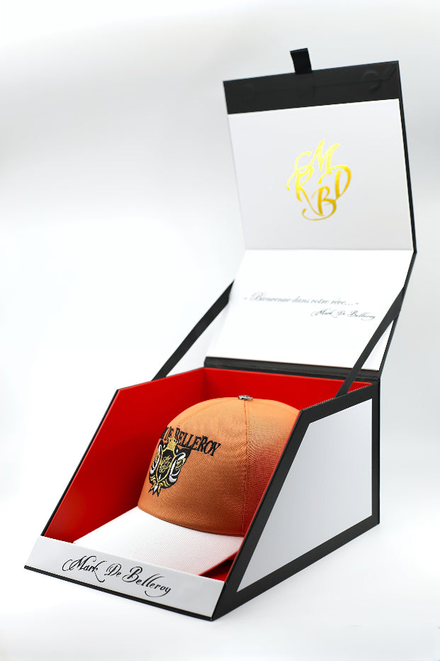 Casquette baseball luxe pêche et blanc dans son écrin signature Mark De Belleroy, broderie noir blanc et fil d'or 24 carats. Fabrication artisanale française Mark De Belleroy.