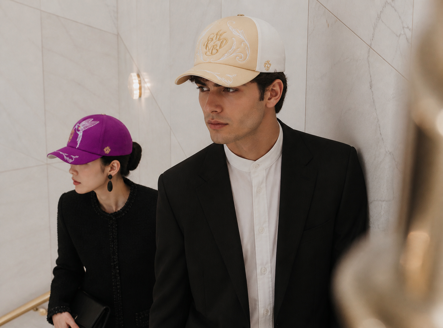 Couple élégant dans un escalier en marbre portant des casquettes de luxe Mark De Belleroy, univers de la mode française haut de gamme