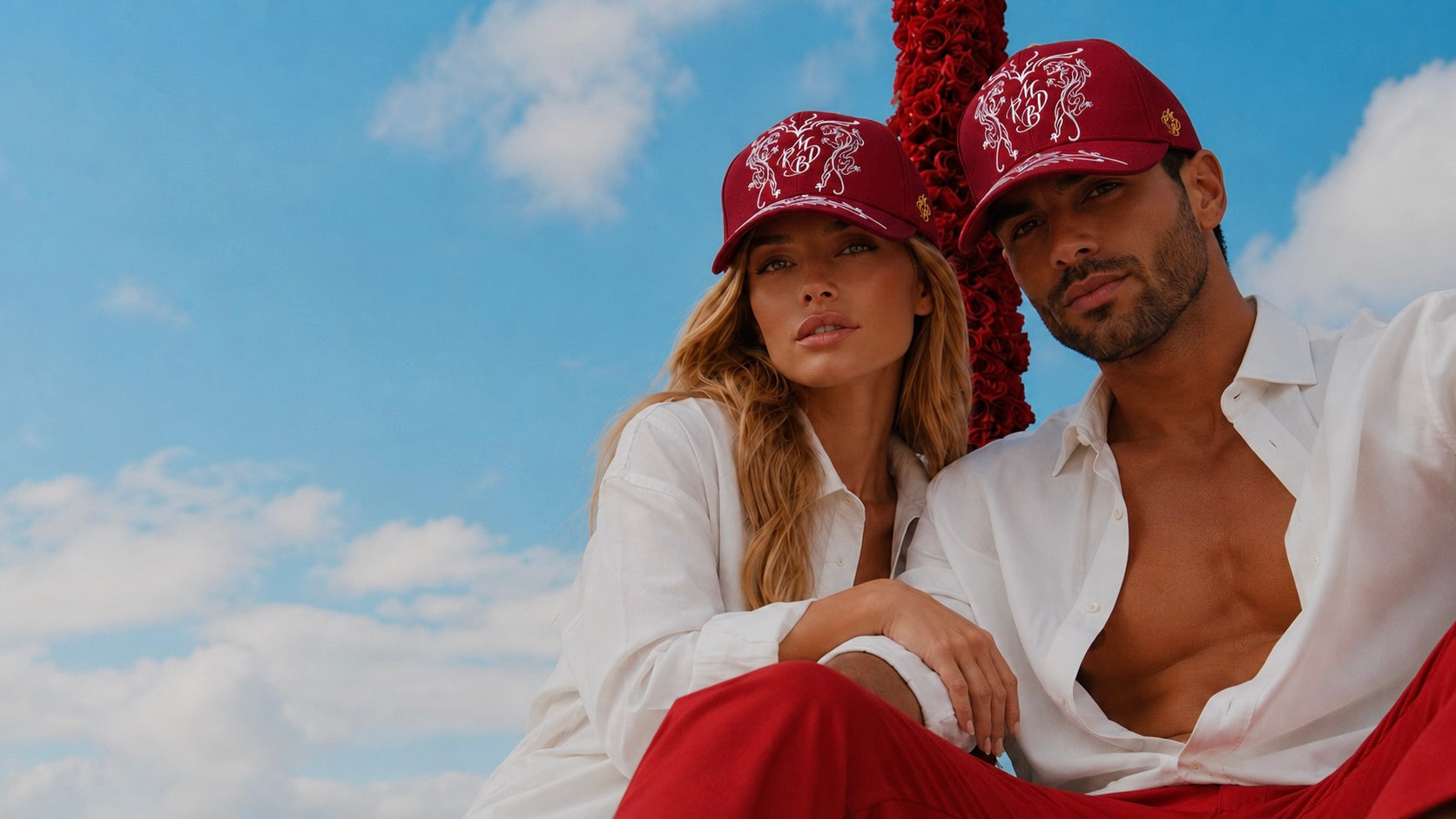 couple chic avec une casquette baseball haut de gamme et luxe Mark De Belleroy, casquette bordeaux, femme blonde et homme brun en chemise blanche et pantalon rouge. casquette française faite à main. Maison de luxe française, casquette French designer