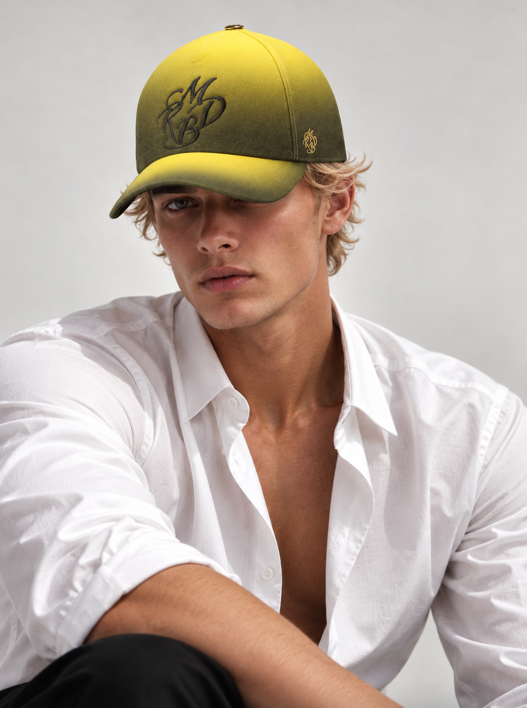 Homme blond portant une casquette haut de gamme et casquette de luxe jaune et noir dégradée de couleur de la maison française Mark De Belleroy. 